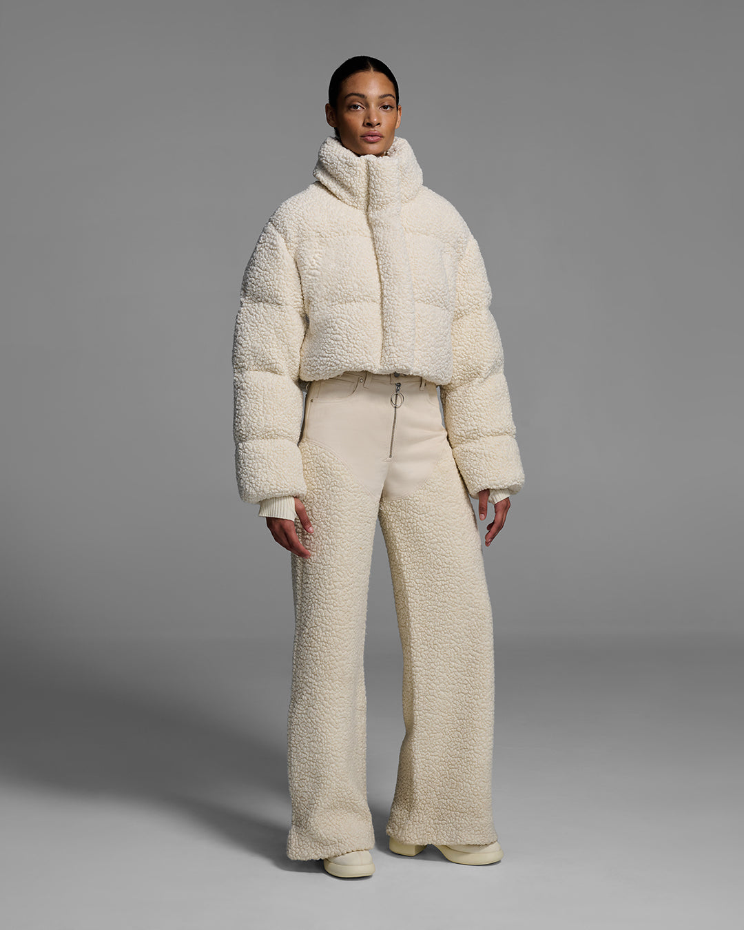 Female model wearing a natural, off-white, sherpa puffer and matching pant on a gray background. #color_natural