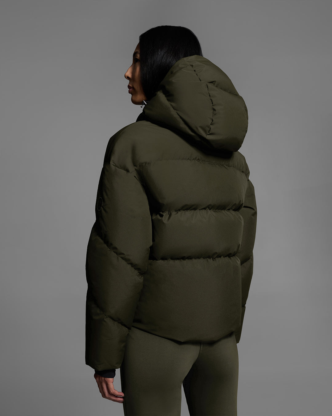 Back view of a female model wearing a classic down filled ski jacket in khaki green with a matching ski pant. #color_khaki