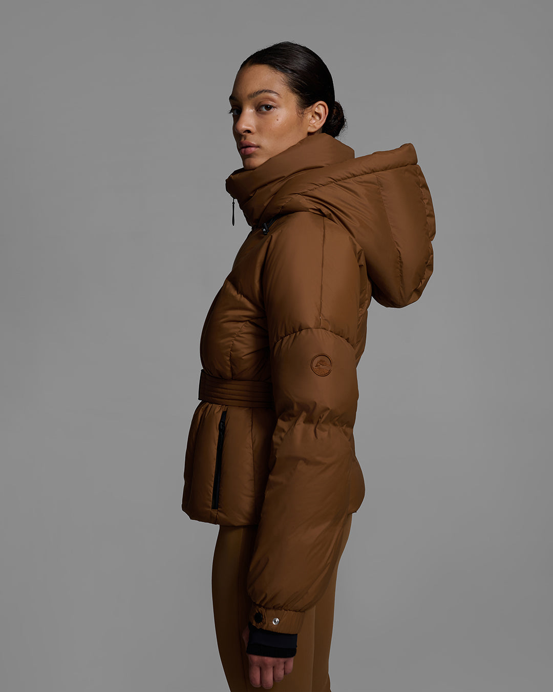 Side view of a female model wearing a classic slope style down filled, belted ski jacket in sepia brown color with a matching ski pant. #color_sepia