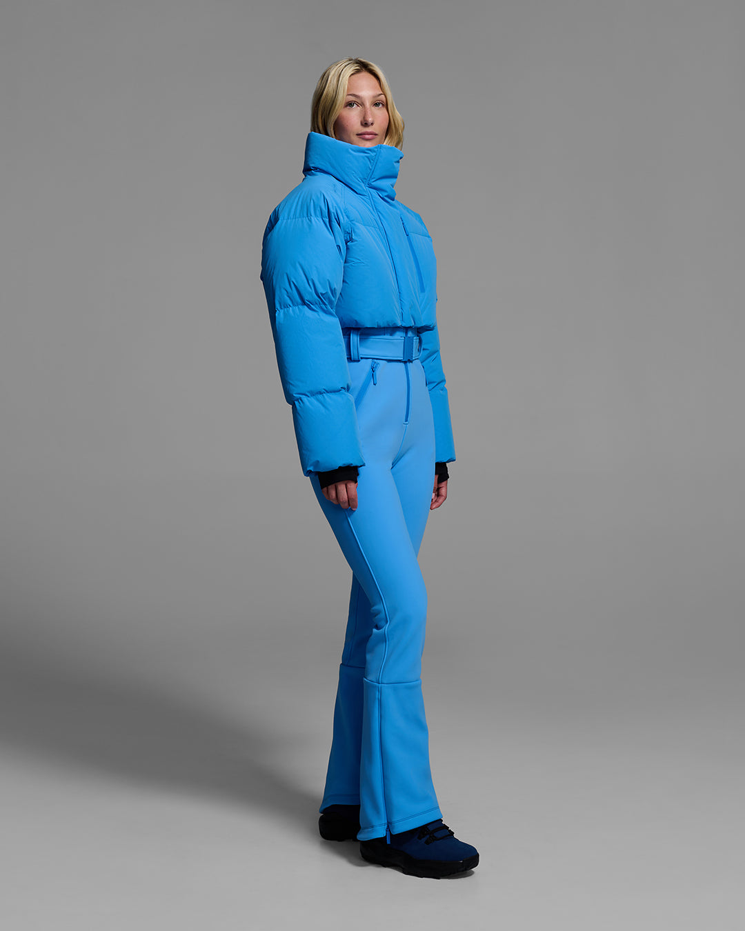 Female model wearing an bright blue ski suit with a puffer crop top, belted waist, and 4-way stretch pant. #color_azul