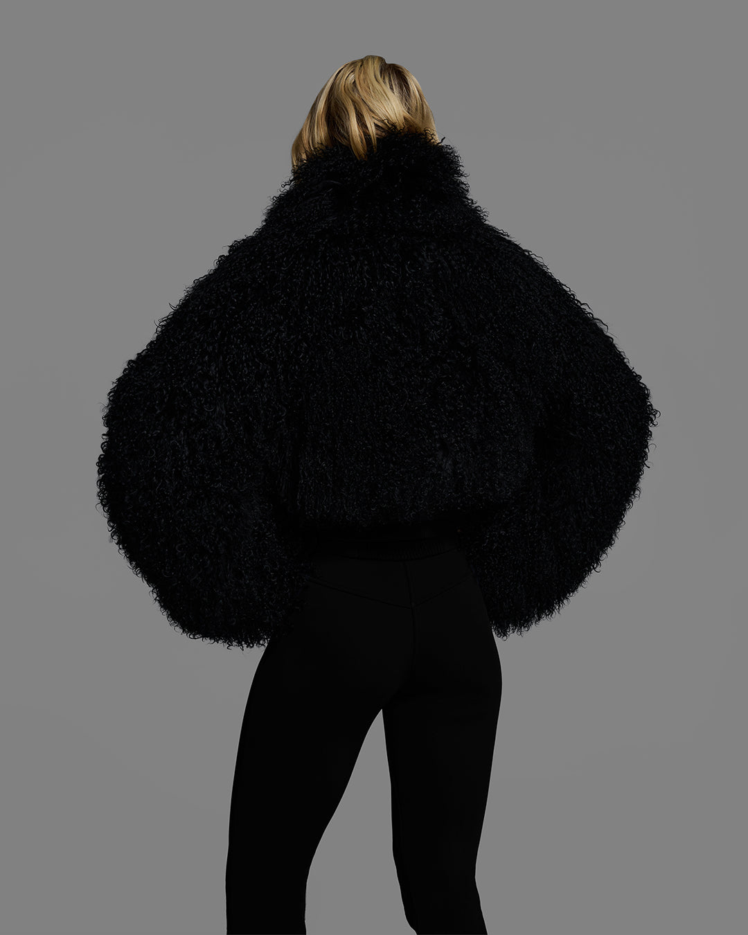 Back view of a female model wearing a black color shearling jacket with matching ski pant. #color_onyx