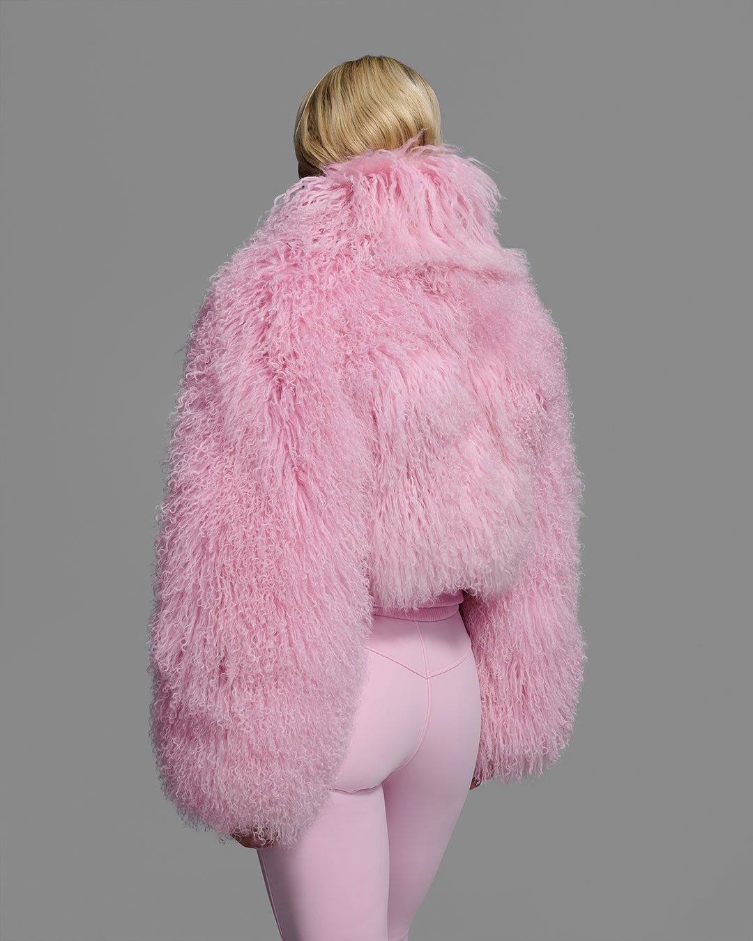 Back view of a female model wearing a natural shearling jacket in peony pink with matching ski pant. #color_peony