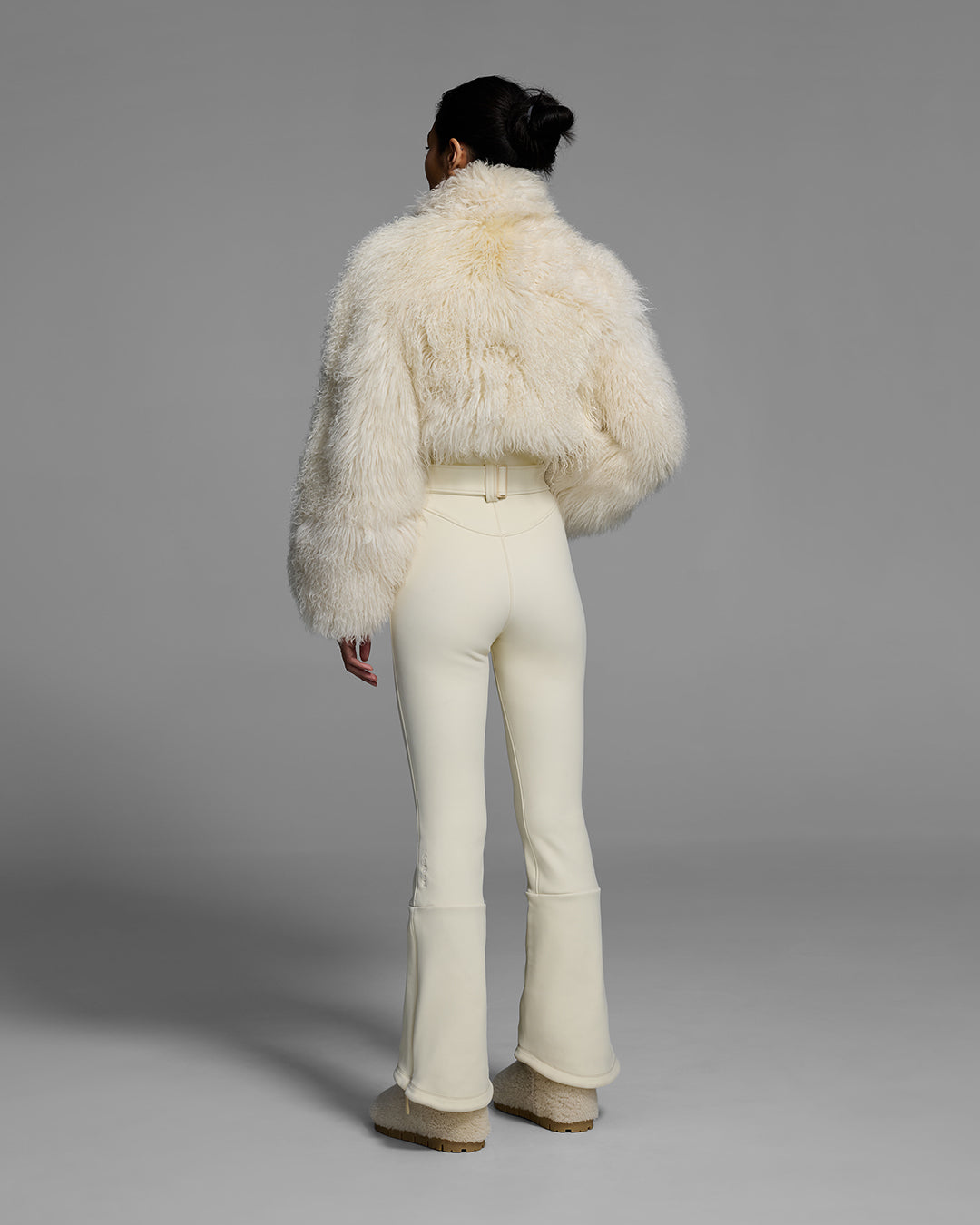 Back view of a woman wearing an alabaster white color ski suit with a shearling top, belted waist, and 4-way stretch pant. #color_alabaster