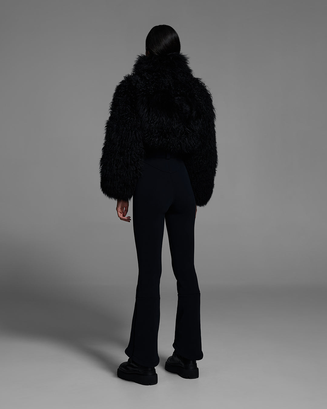 Back view of a woman wearing an alabaster white color ski suit with a shearling top, belted waist, and 4-way stretch pant. #color_onyx