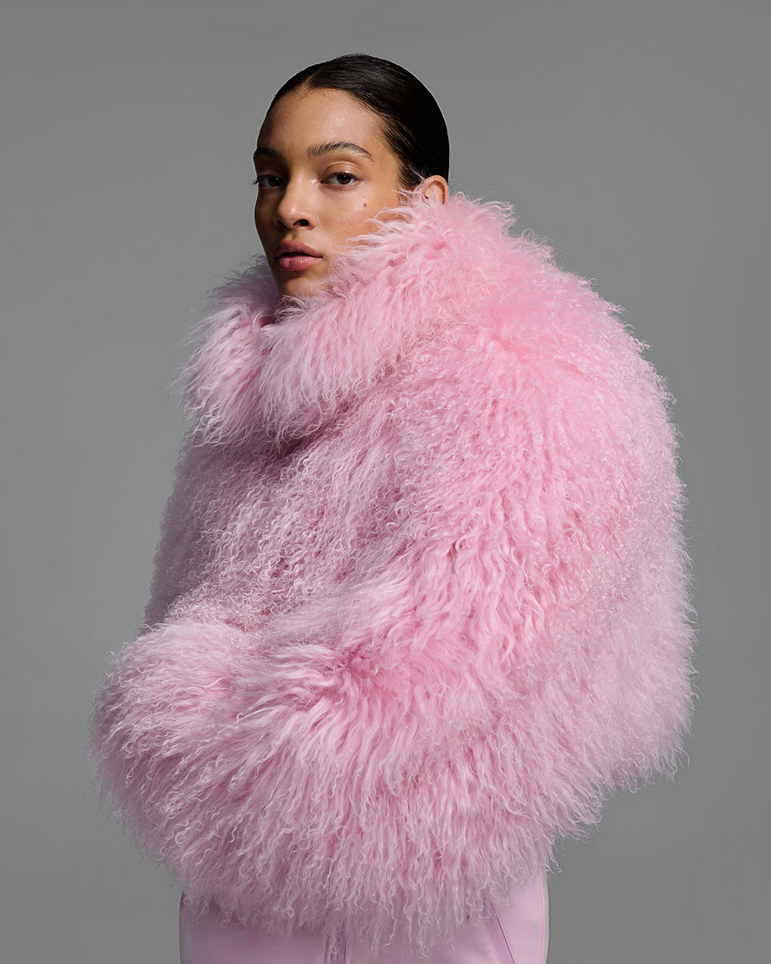 Detail side view of a woman wearing an peony pink color ski suit with a shearling top, belted waist, and 4-way stretch pant. #color_peony