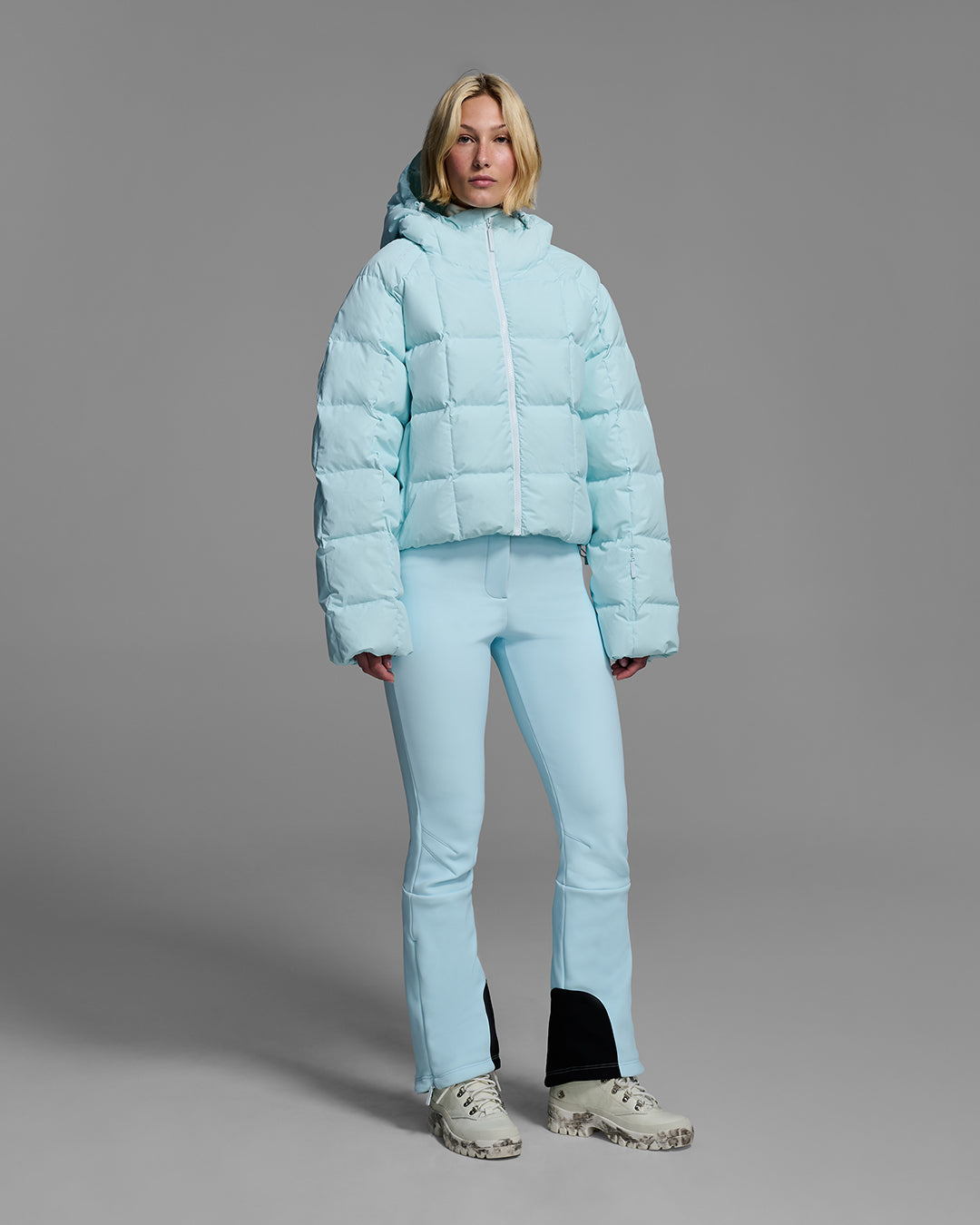 Woman wearing an iceberg blue color quilted down ski jacket with matching ski pants. #color_iceberg