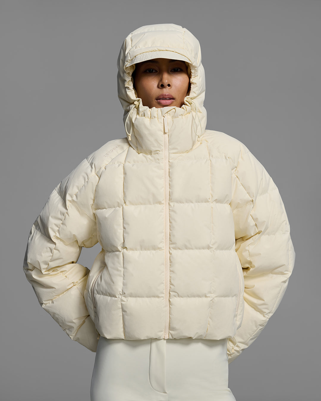 Front detail view of a woman wearing an off-white color quilted down ski jacket with matching ski pants. #color_alabaster