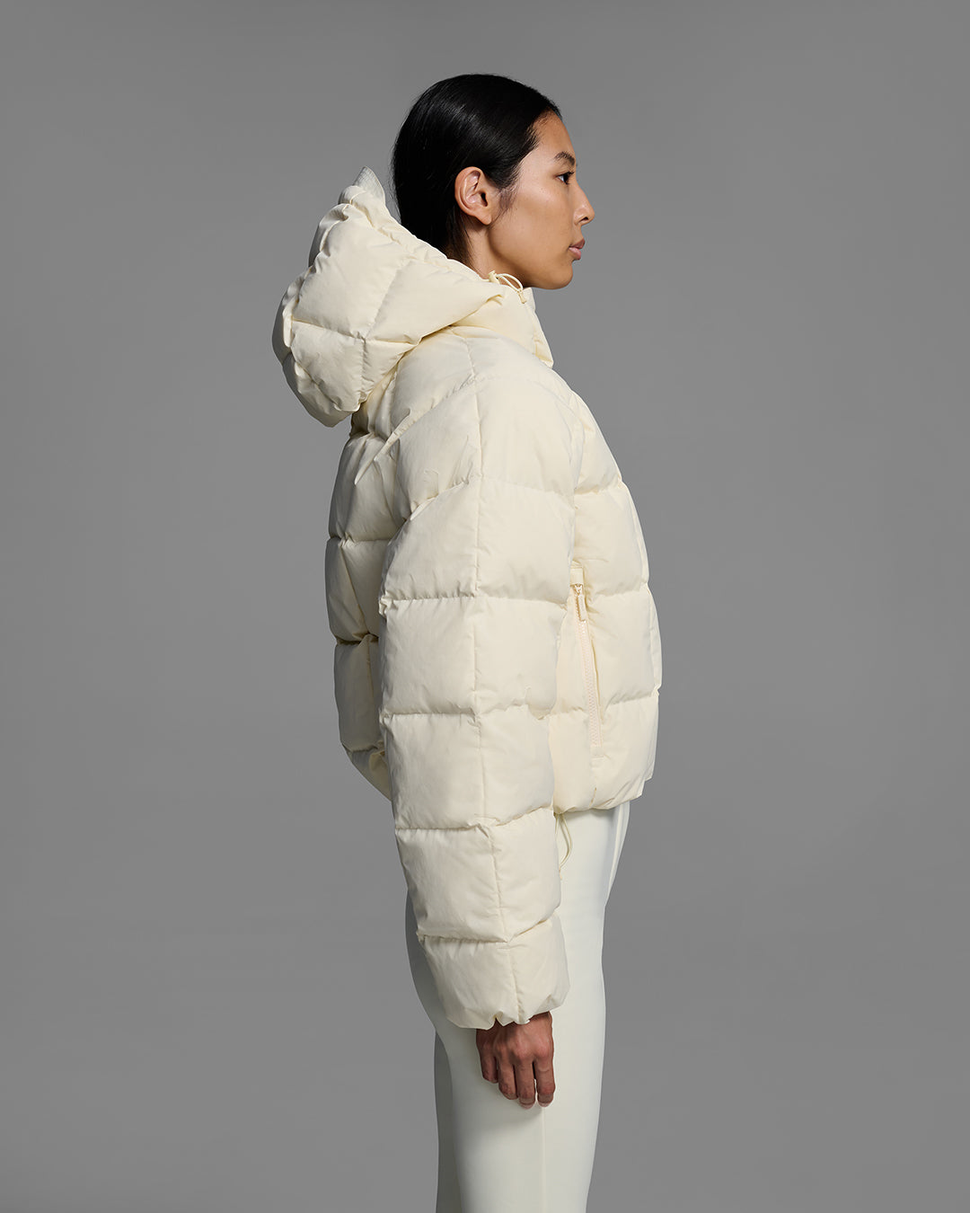 Side view of a woman wearing an off-white color quilted down ski jacket with matching ski pants. #color_alabaster