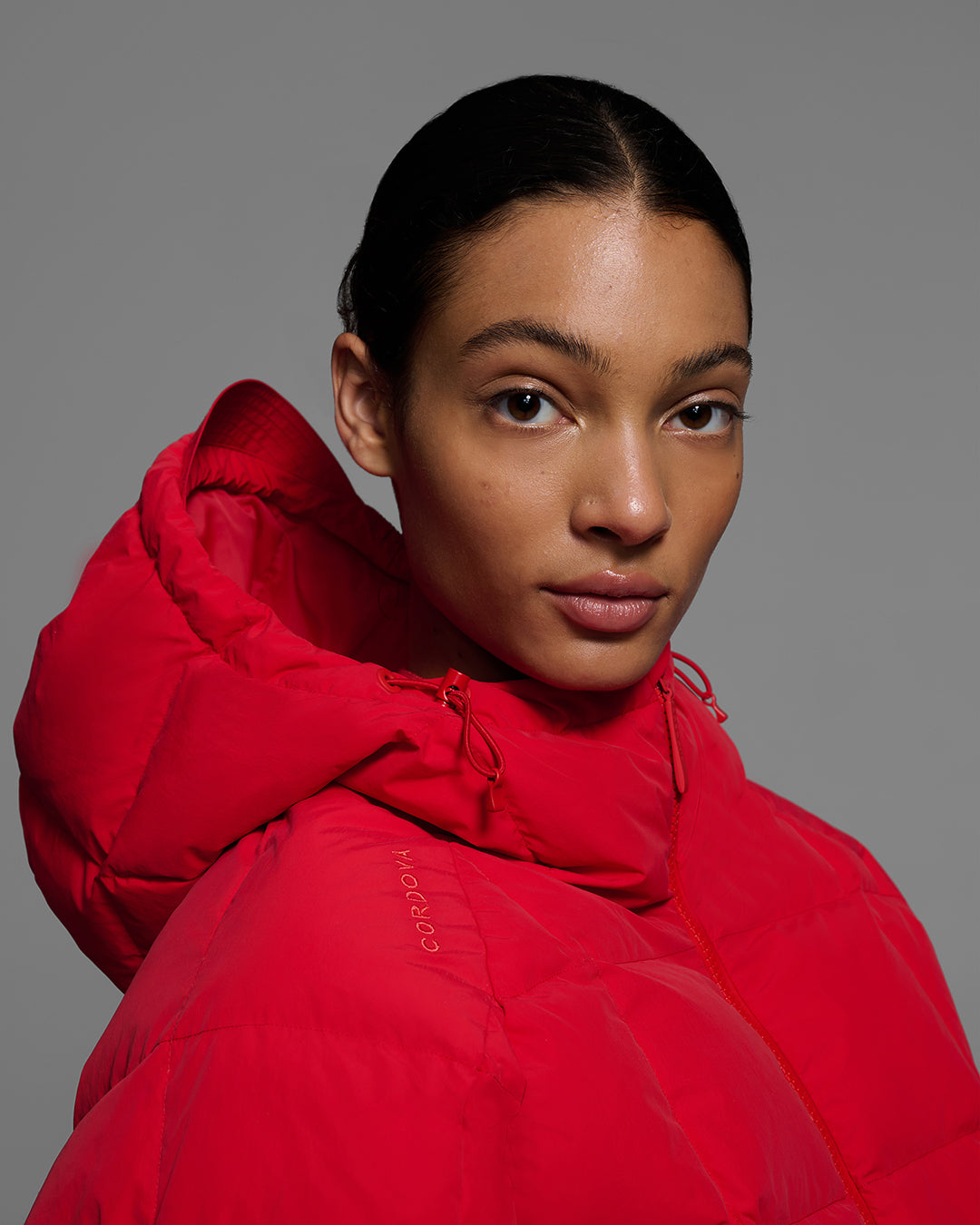 Detail view from the shoulder up of a woman wearing a bright poppy red color quilted down ski jacket. #color_poppy
