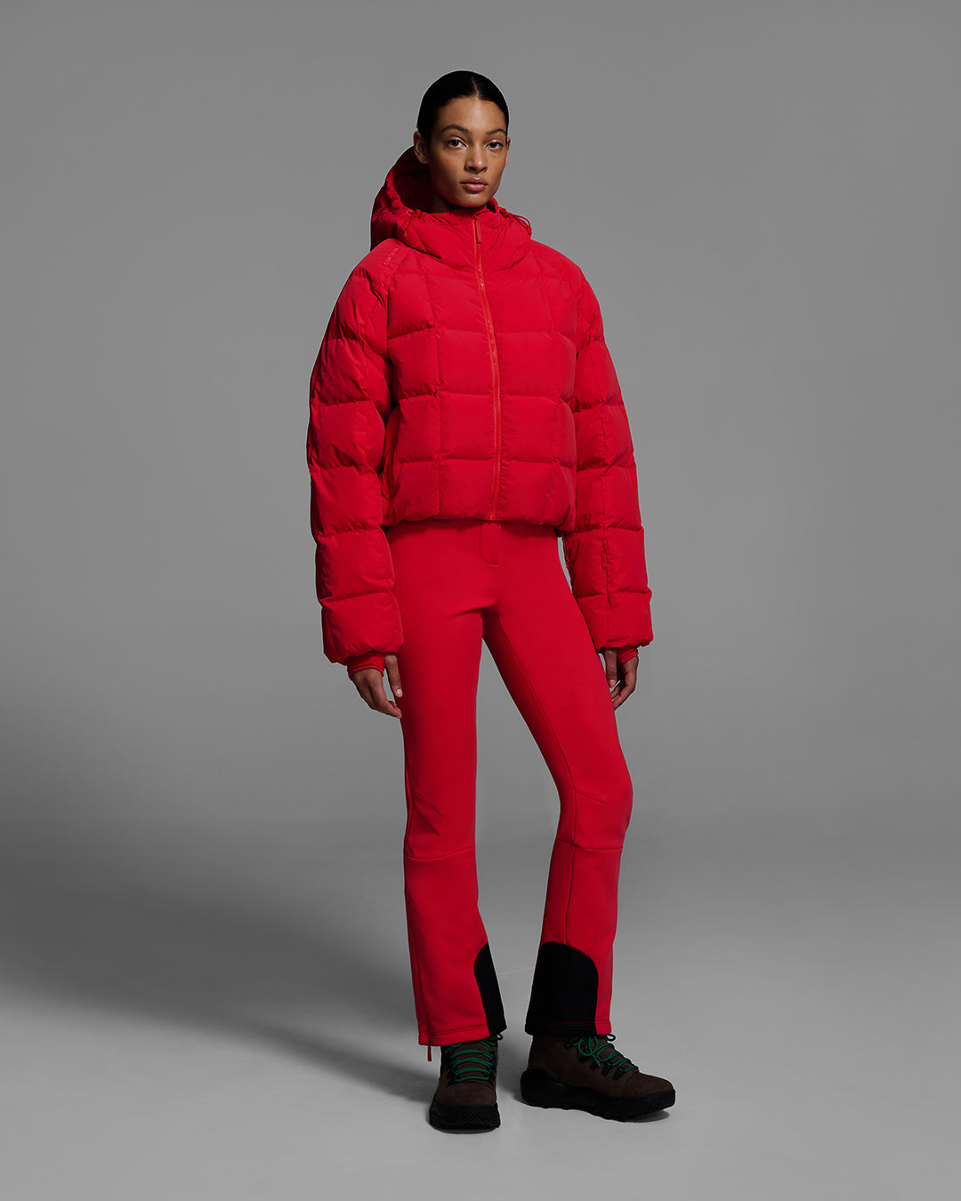 Woman wearing a bright poppy red color quilted down ski jacket with matching ski pants. #color_poppy