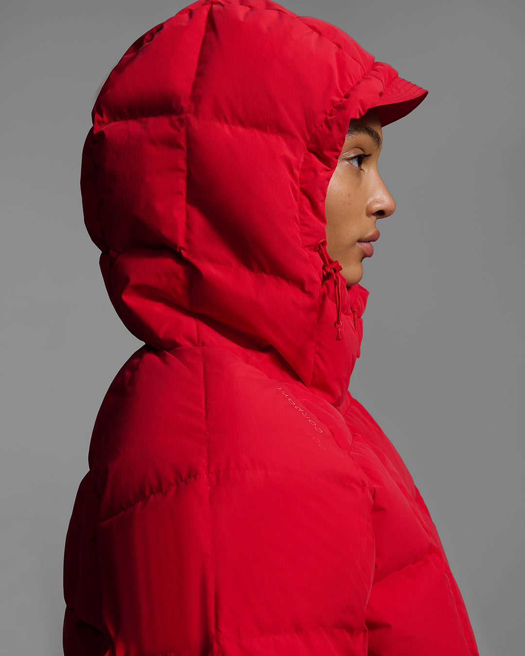 Detail of focused on the hood of a down quilted ski jacket in poppy red color worn by a woman. #color_poppy
