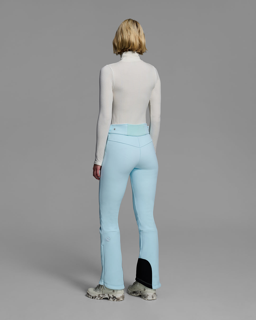 Back view of a woman wearing a 4-way stretch ski pant in iceberg blue and a white base layer top. #color_iceberg