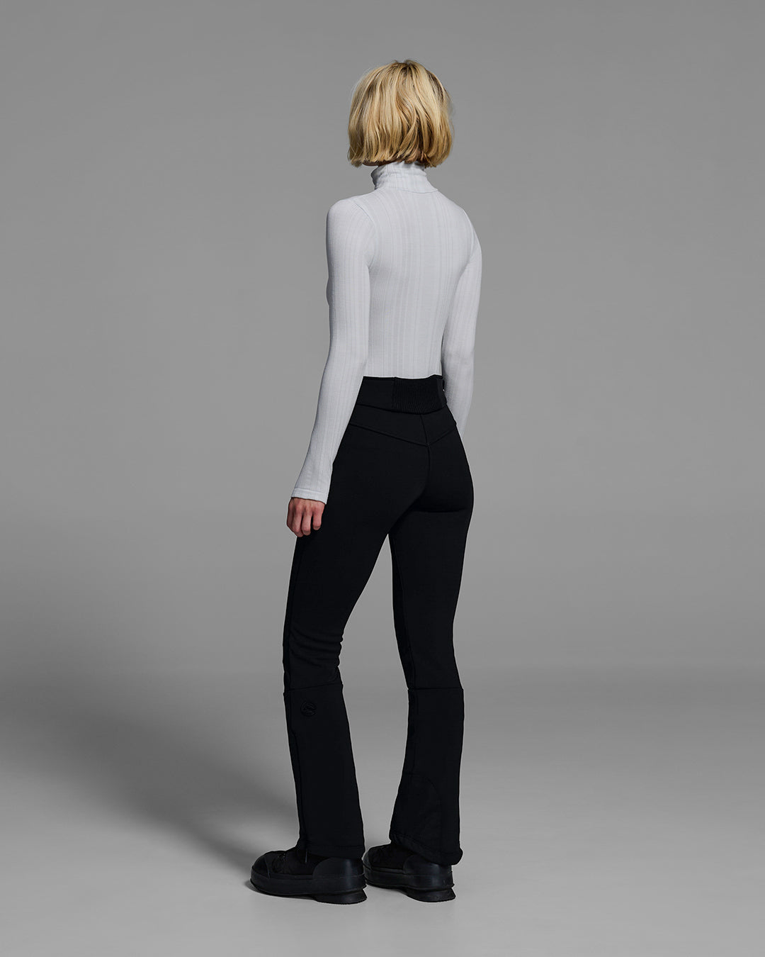 Back view of a woman wearing a 4-way stretch ski pant in black with a gray base layer top. #color_onyx