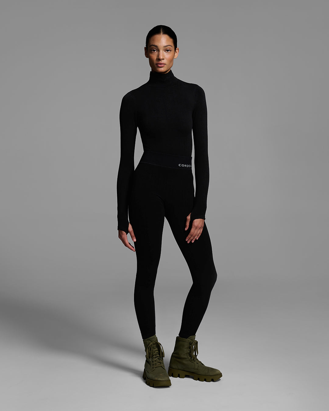 Woman wearing a black turtleneck and matching pant base layer set made of merino wool blend. #color_onyx