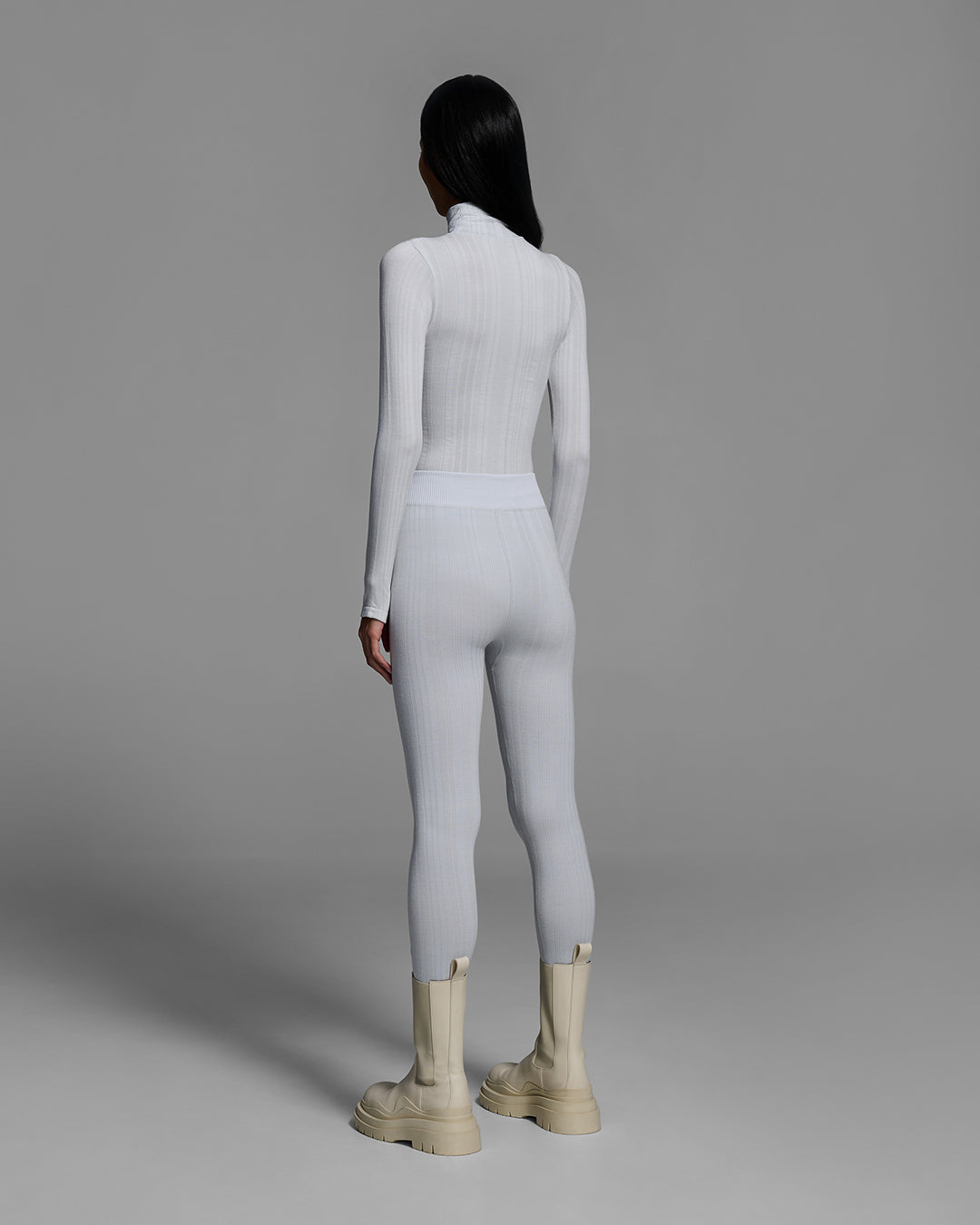 Back view of a woman wearing a smoke gray color turtleneck and matching pant base layer set made of merino wool blend. #color_smoke