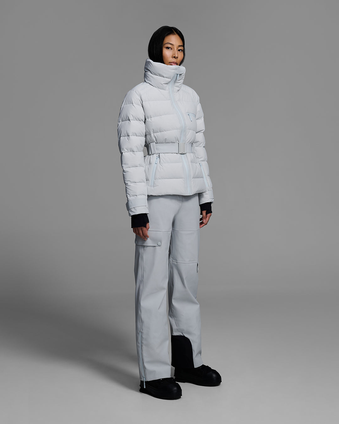 Woman wearing a belted down-fill puffer ski jacket in smoke gray with matching pant and black shoes. #color_smoke