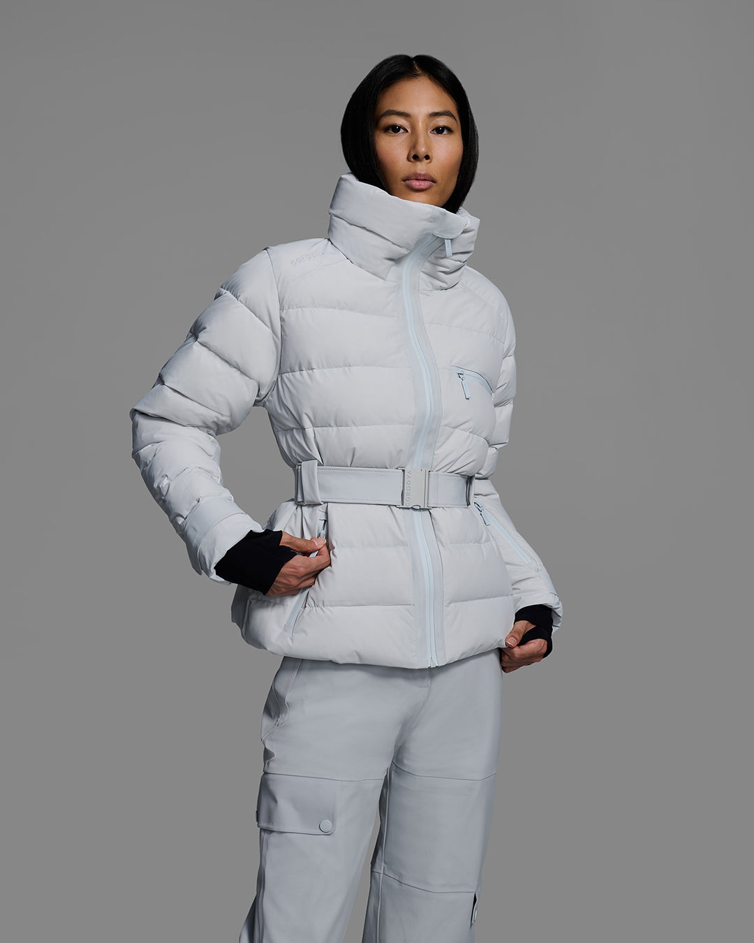 Front detail view of a woman wearing a belted down-fill puffer ski jacket in smoke gray with matching pant. #color_smoke