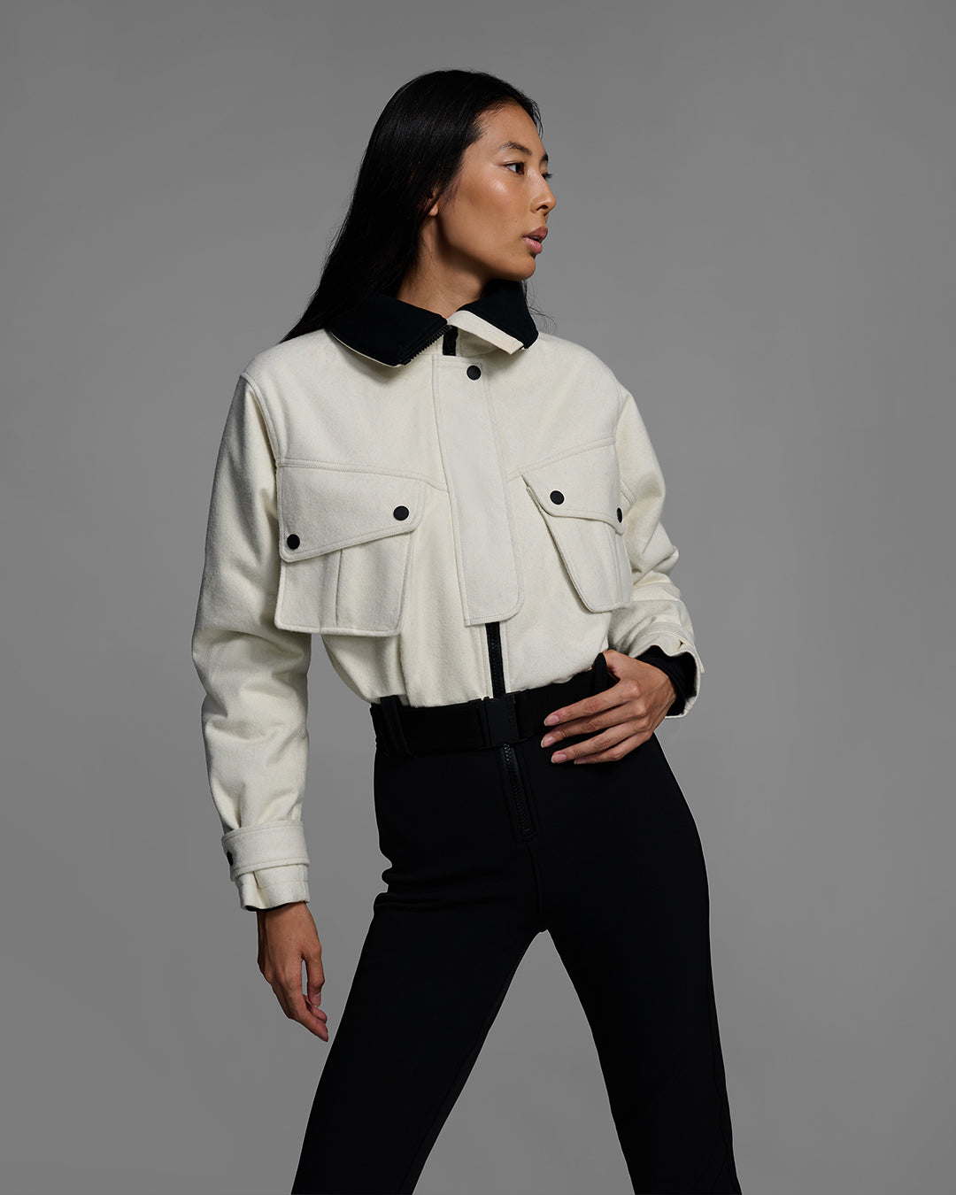 Detail front view of a woman wearing a natural white color wool top ski suit with belted waist and black 4-way stretch bottom. #color_natural / onyx