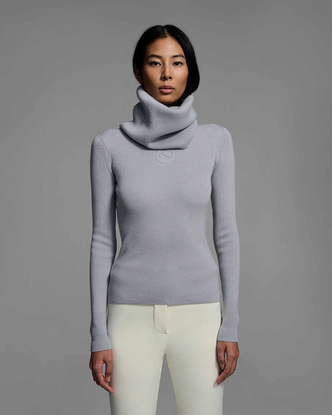 Woman wearing a gray melange ski buff made of merino wool with matching sweater and white ski pant. #color_gray melange