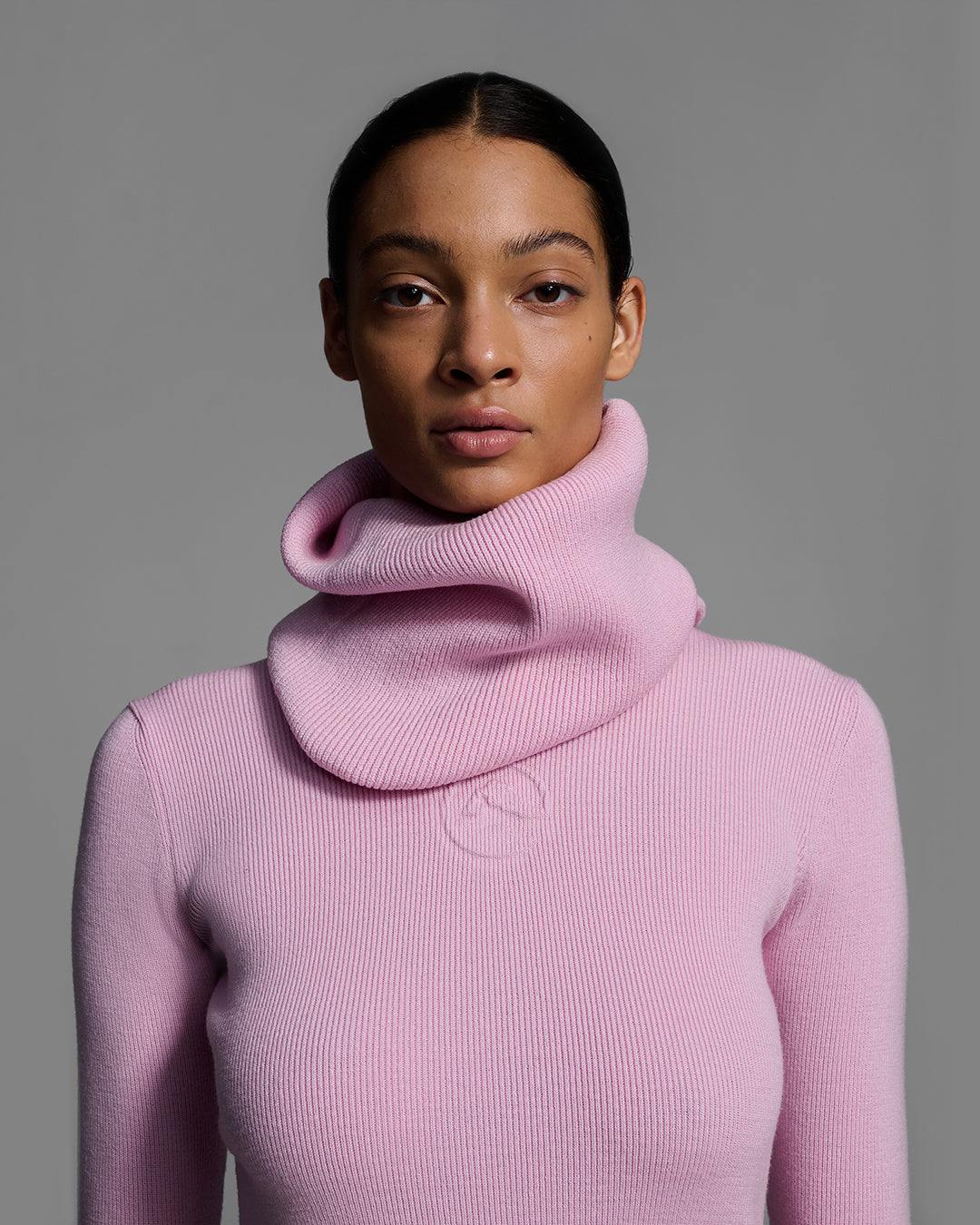 Close up of a woman wearing a peony pink color ski buff made of merino wool with matching sweater. #color_peony