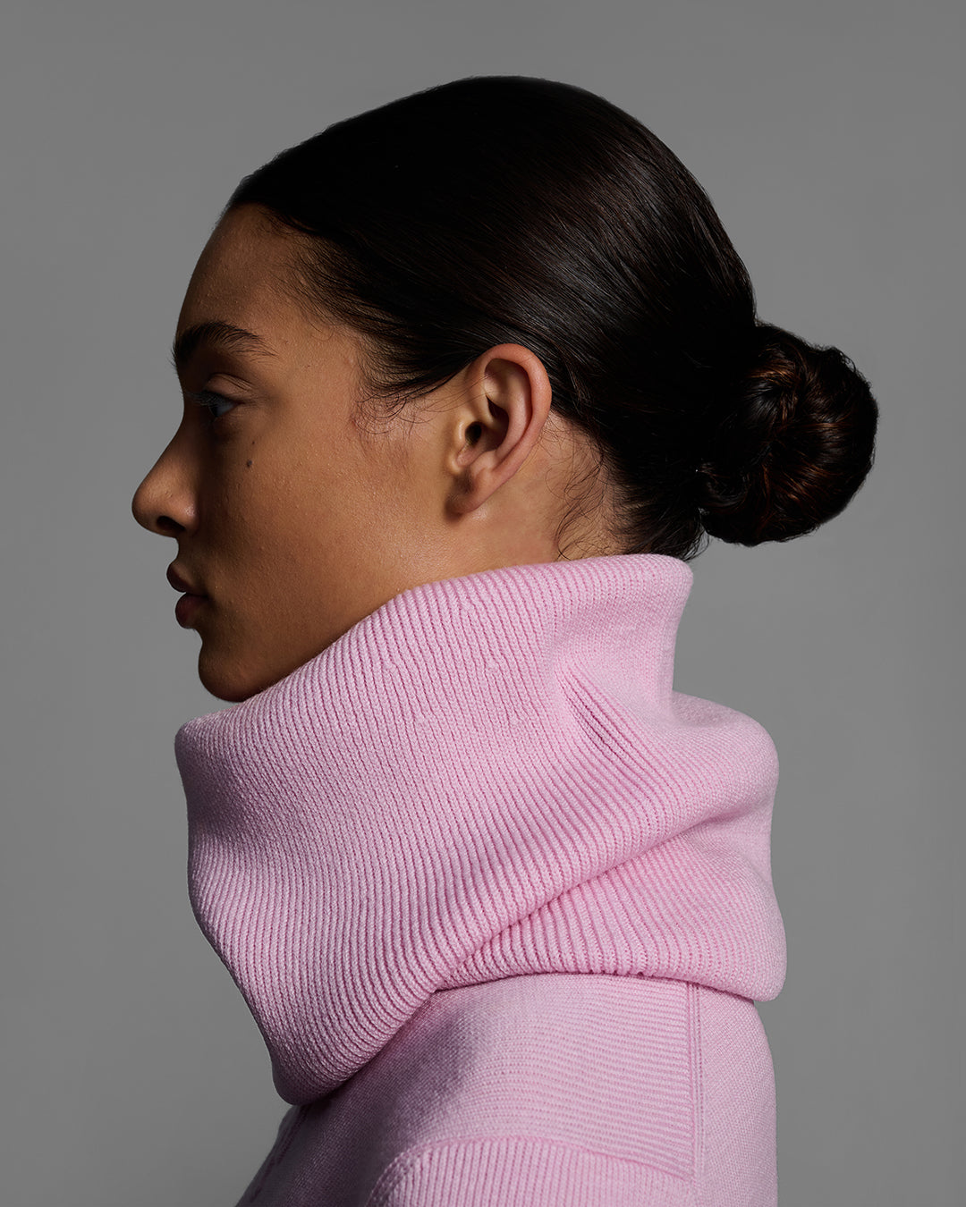 Side view close up of a woman wearing a peony pink color ski buff made of merino wool with matching sweater. #color_peony