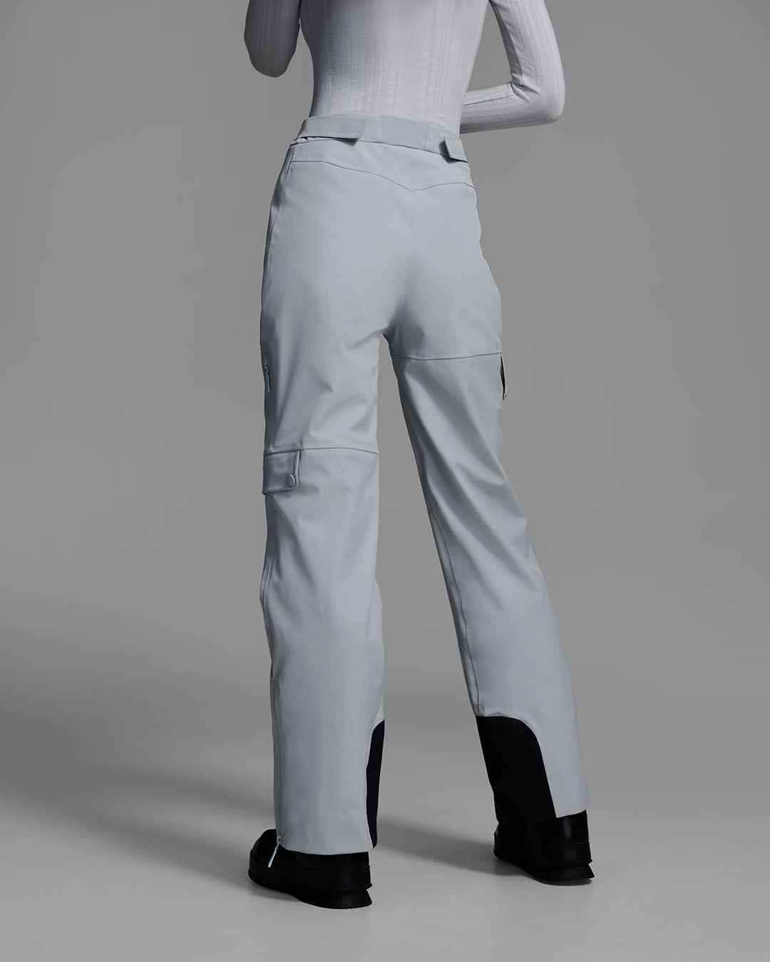 Back view of a woman wearing technical ski pants in smoke gray with matching base layer top. #color_smoke