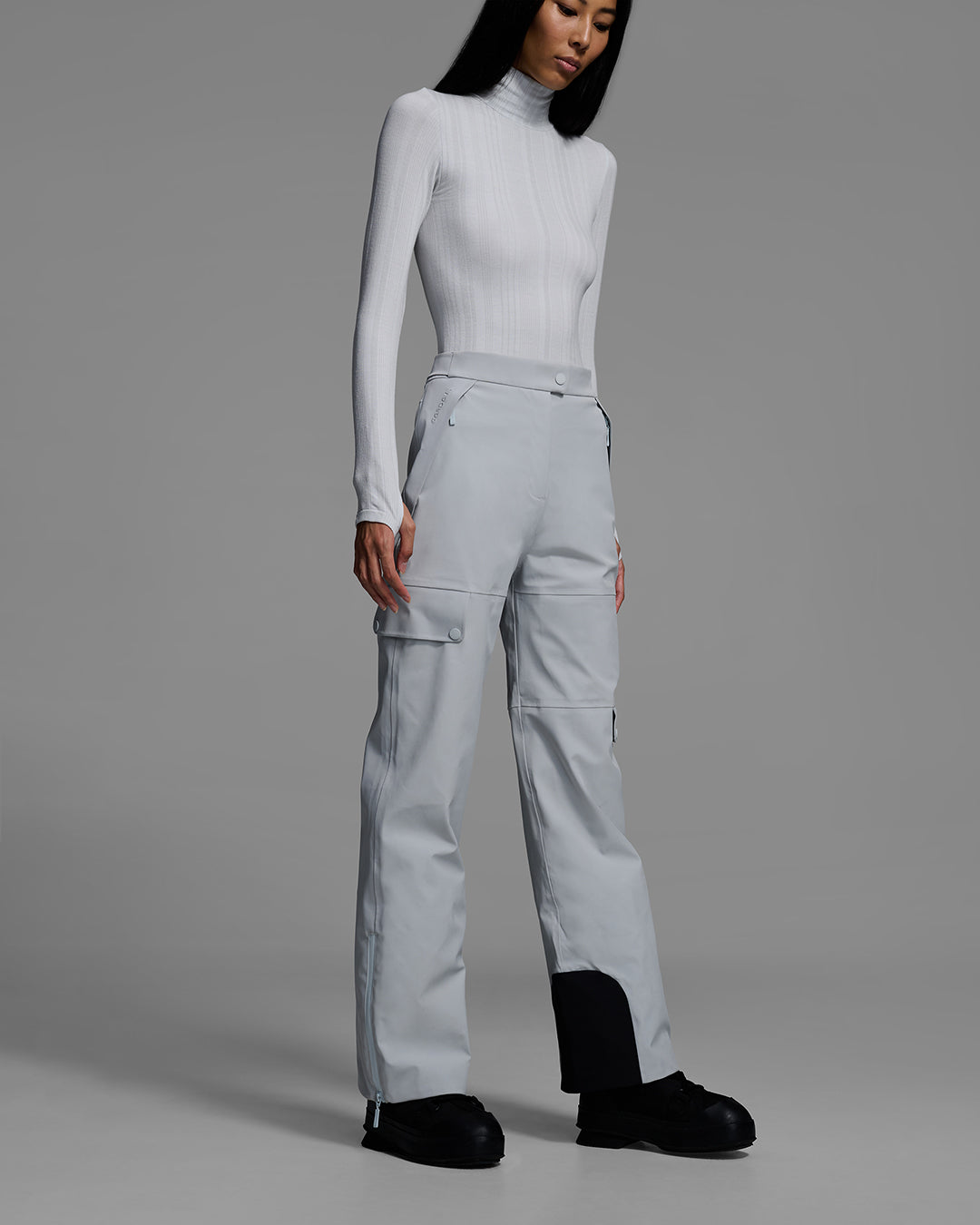 Woman wearing technical ski pants in smoke gray with matching base layer top. #color_smoke